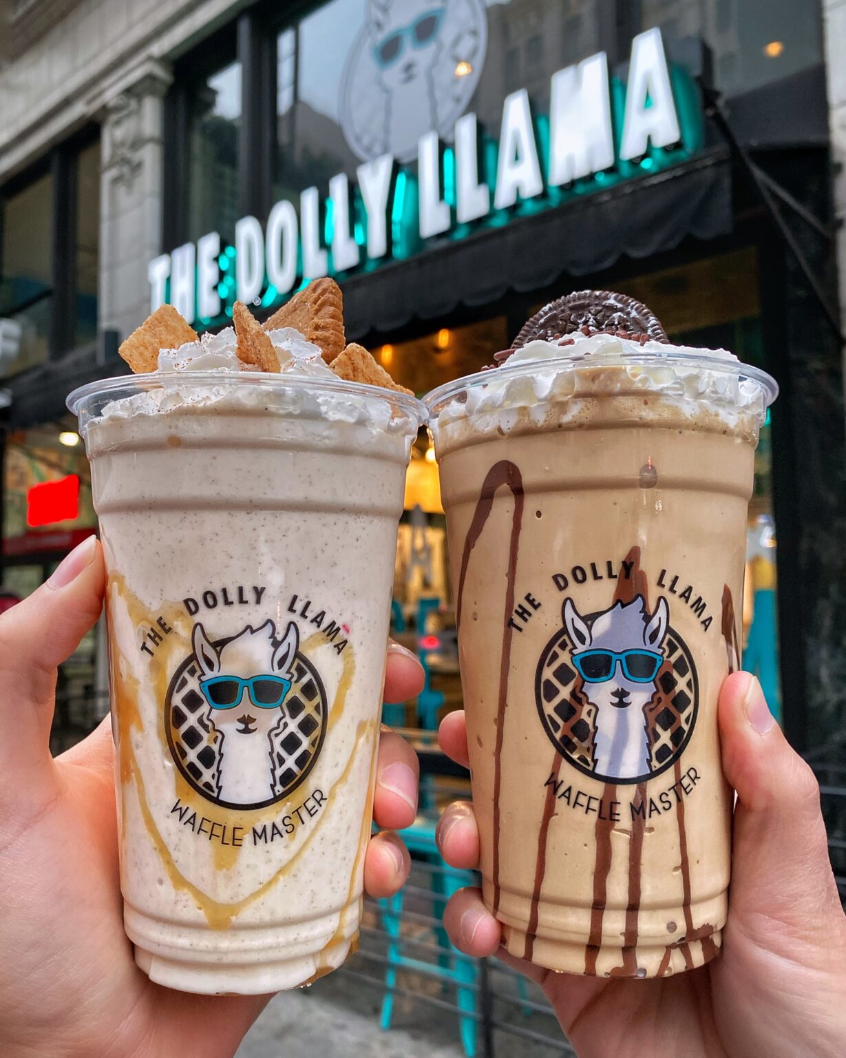 Holding two Dolly Llama milk shakes outside of storefront signage.
